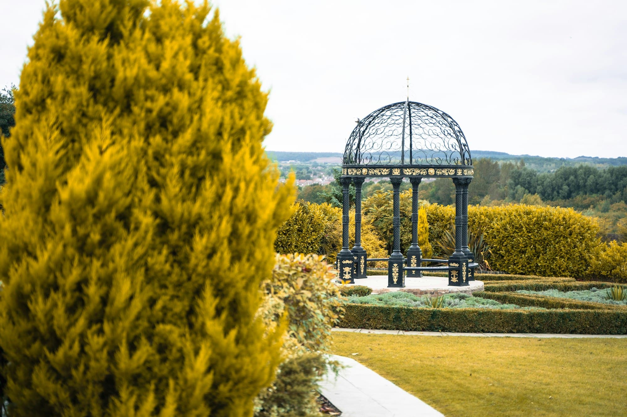Schmiedeeiserner Pavillon in einem gepflegten Garten im goldenen Abendlicht